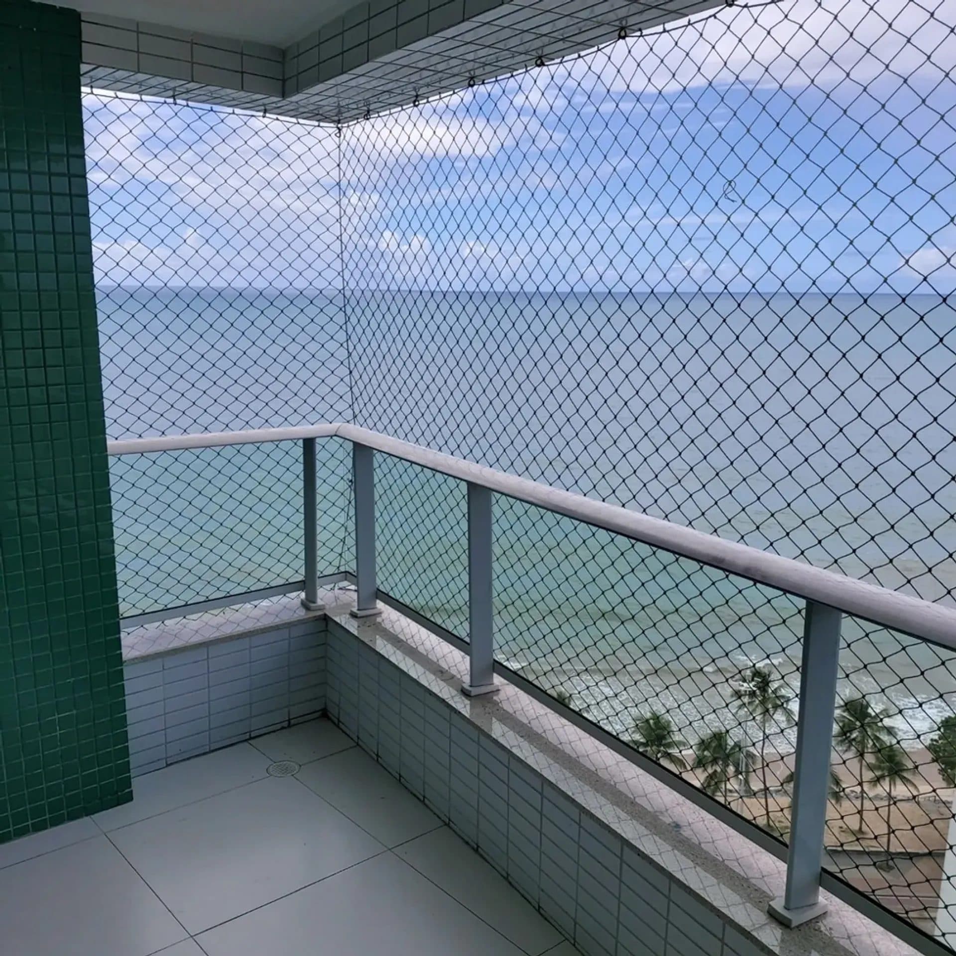 Varanda com piso claro, grade de protecao e vista para o mar